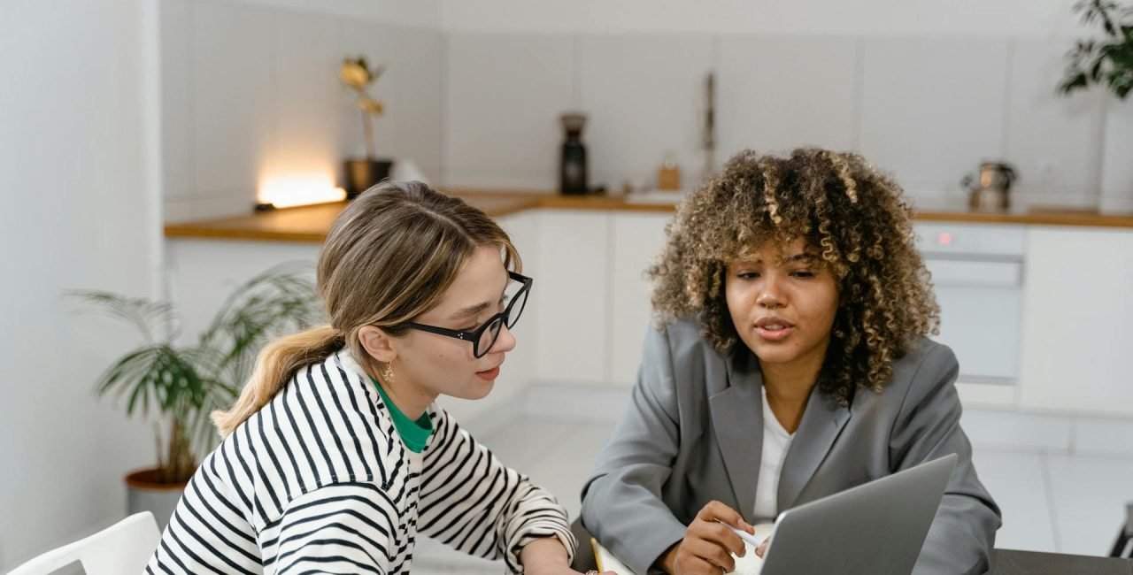 Two women working together on a laptop at a desk.