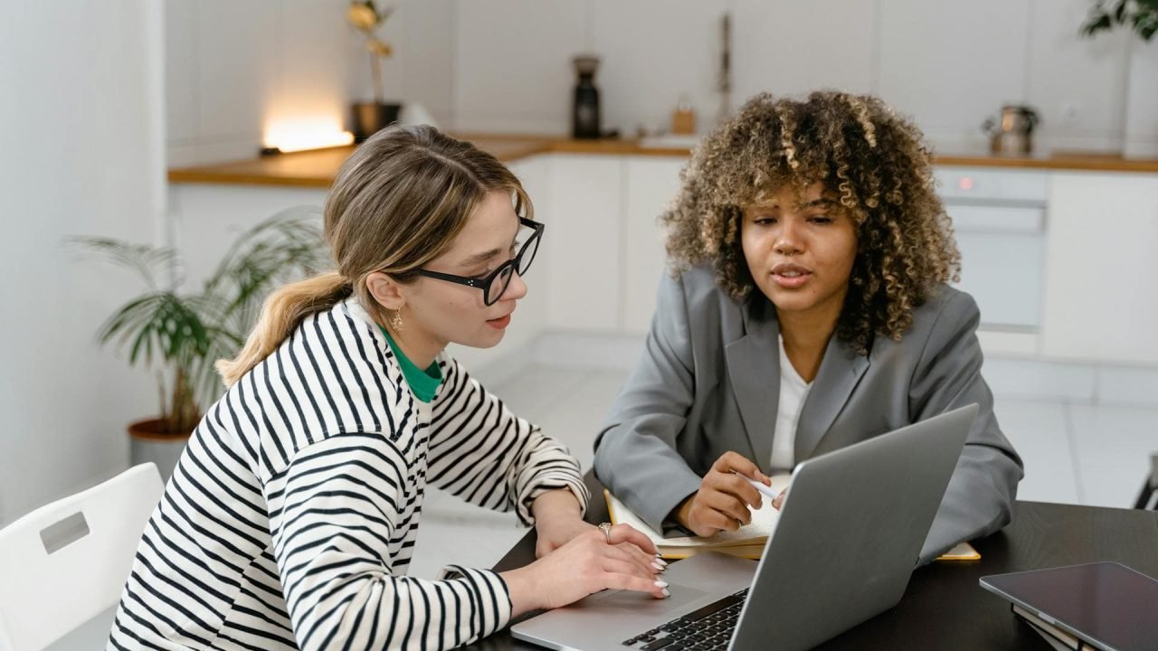 Two women working together on a laptop at a desk.