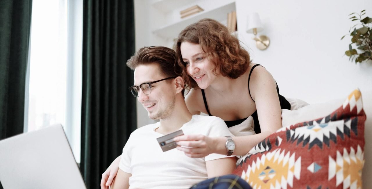 A happy couple browsing products on a laptop, with the woman holding a credit card.