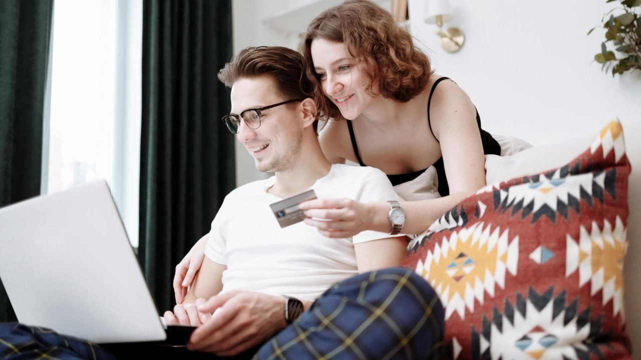 A happy couple browsing products on a laptop, with the woman holding a credit card.