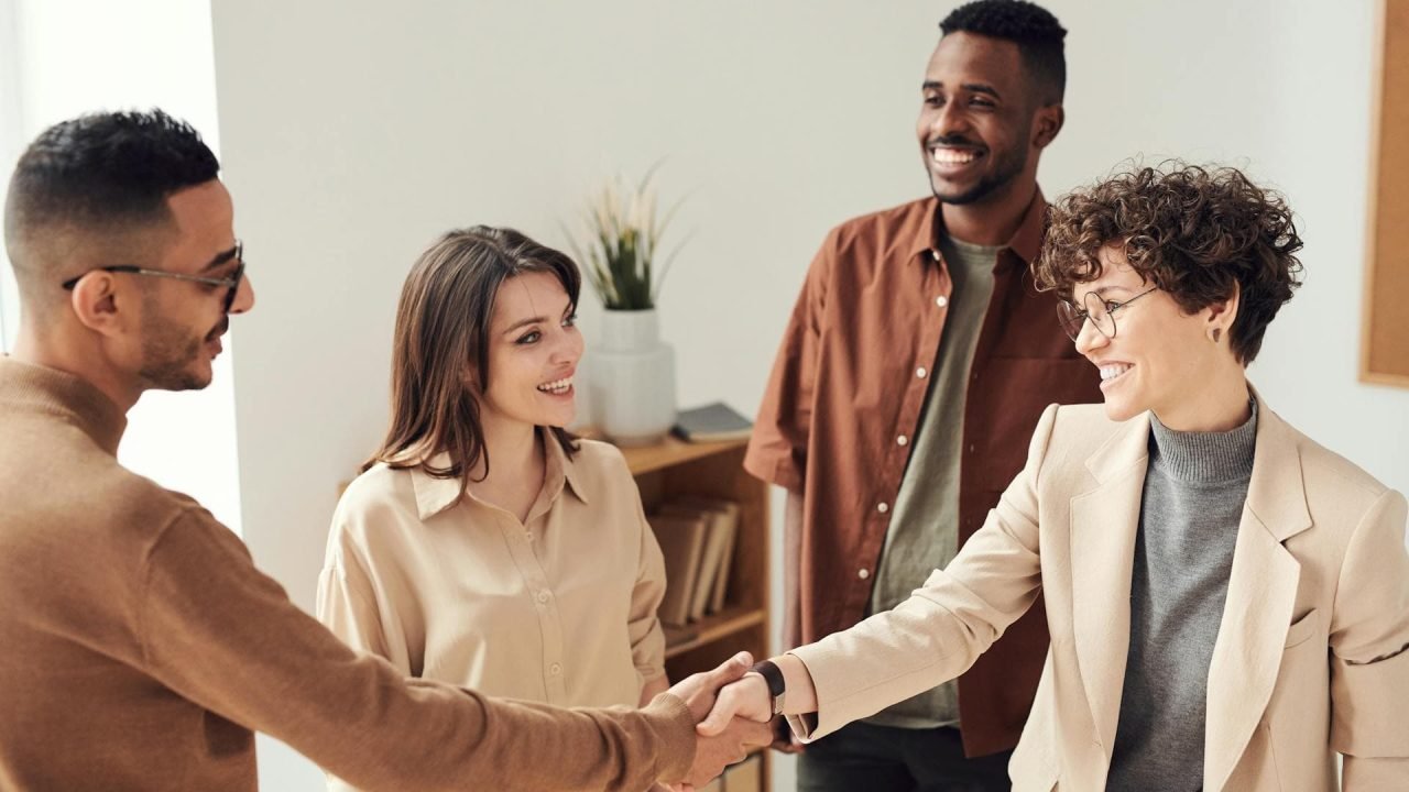 Successful freelance partnership. Happy handshake between freelancer and client, with two other smiling professionals in the background.