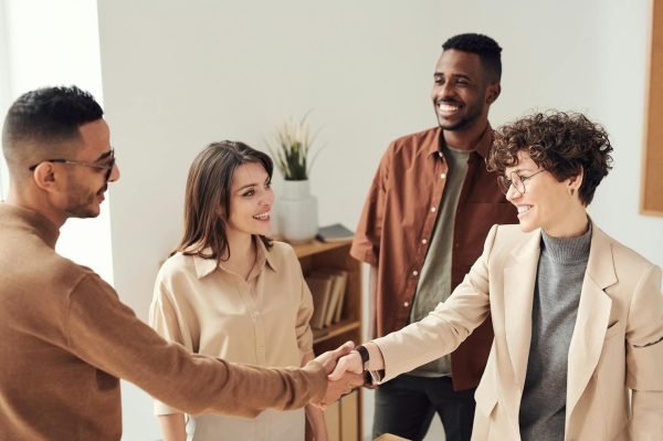 Successful freelance partnership. Happy handshake between freelancer and client, with two other smiling professionals in the background.