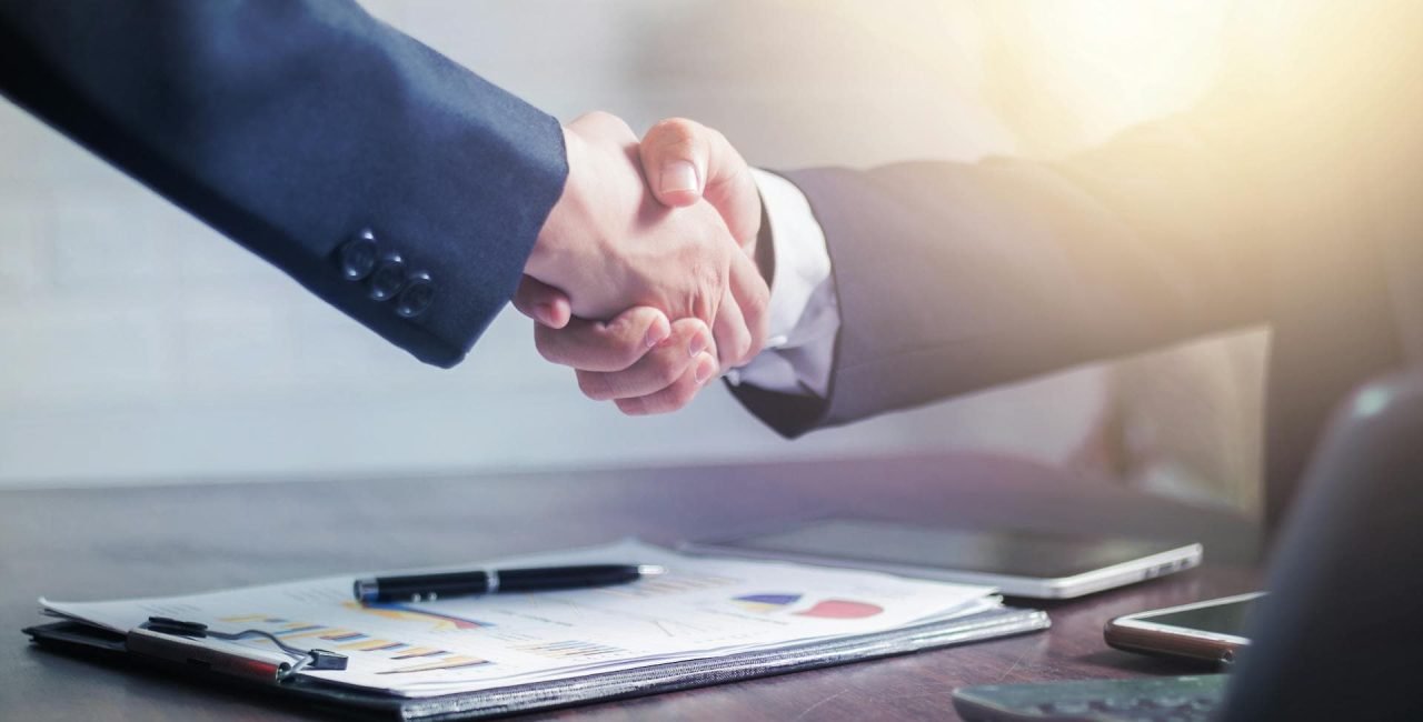 Client and freelancer shaking hands over a proposal on a desk.