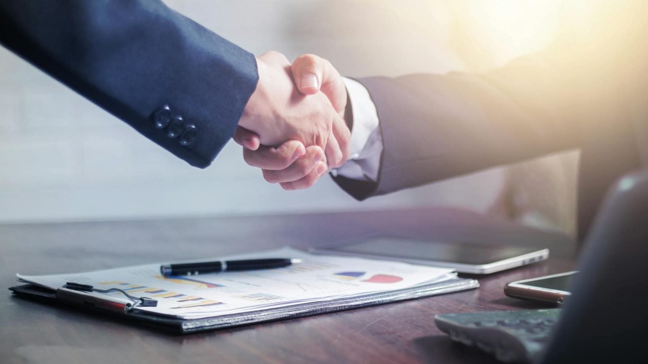 Client and freelancer shaking hands over a proposal on a desk.