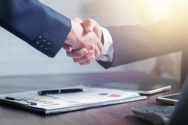 Client and freelancer shaking hands over a proposal on a desk.